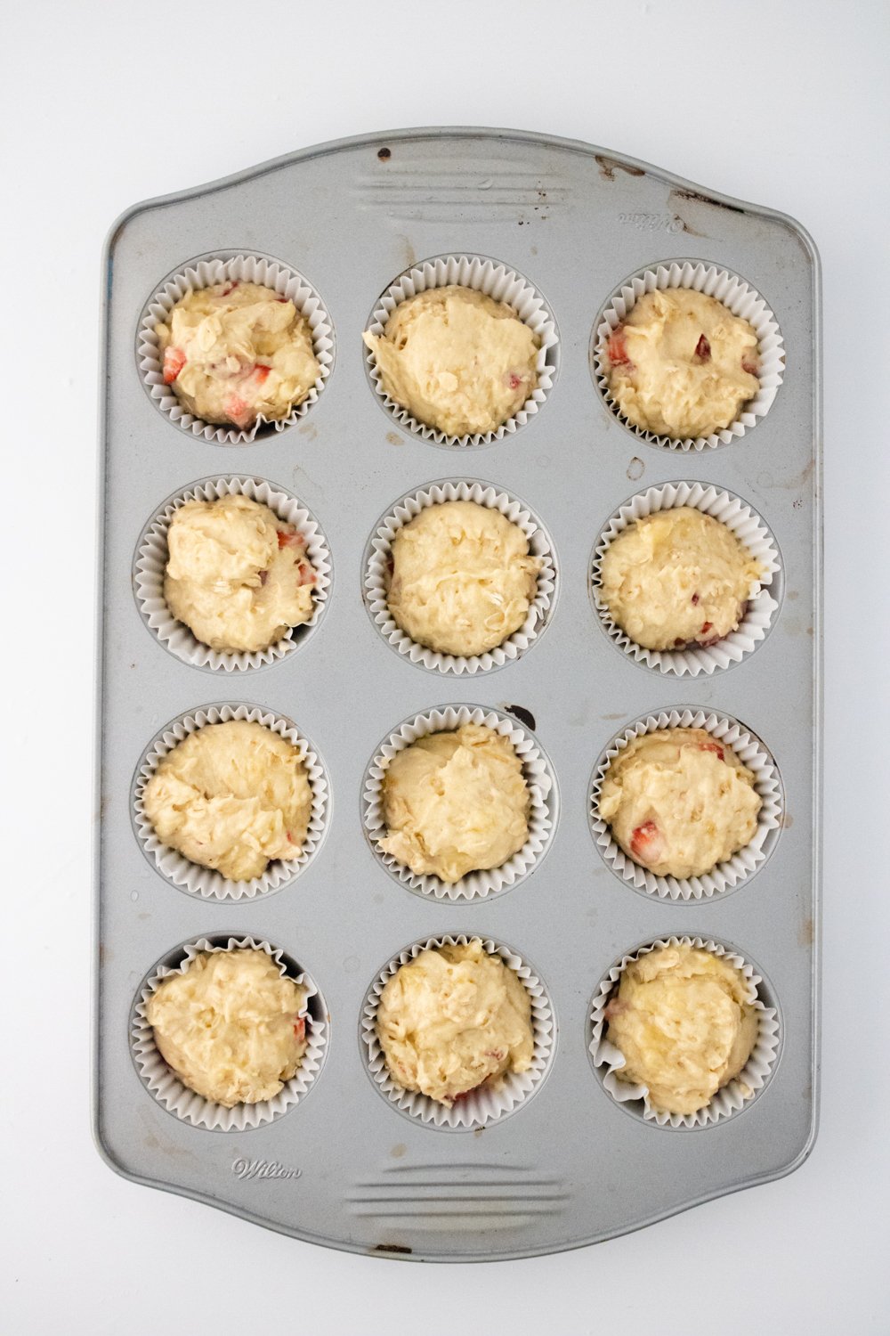 A top-down view of a muffin tin filled with strawberry banana bread batter.