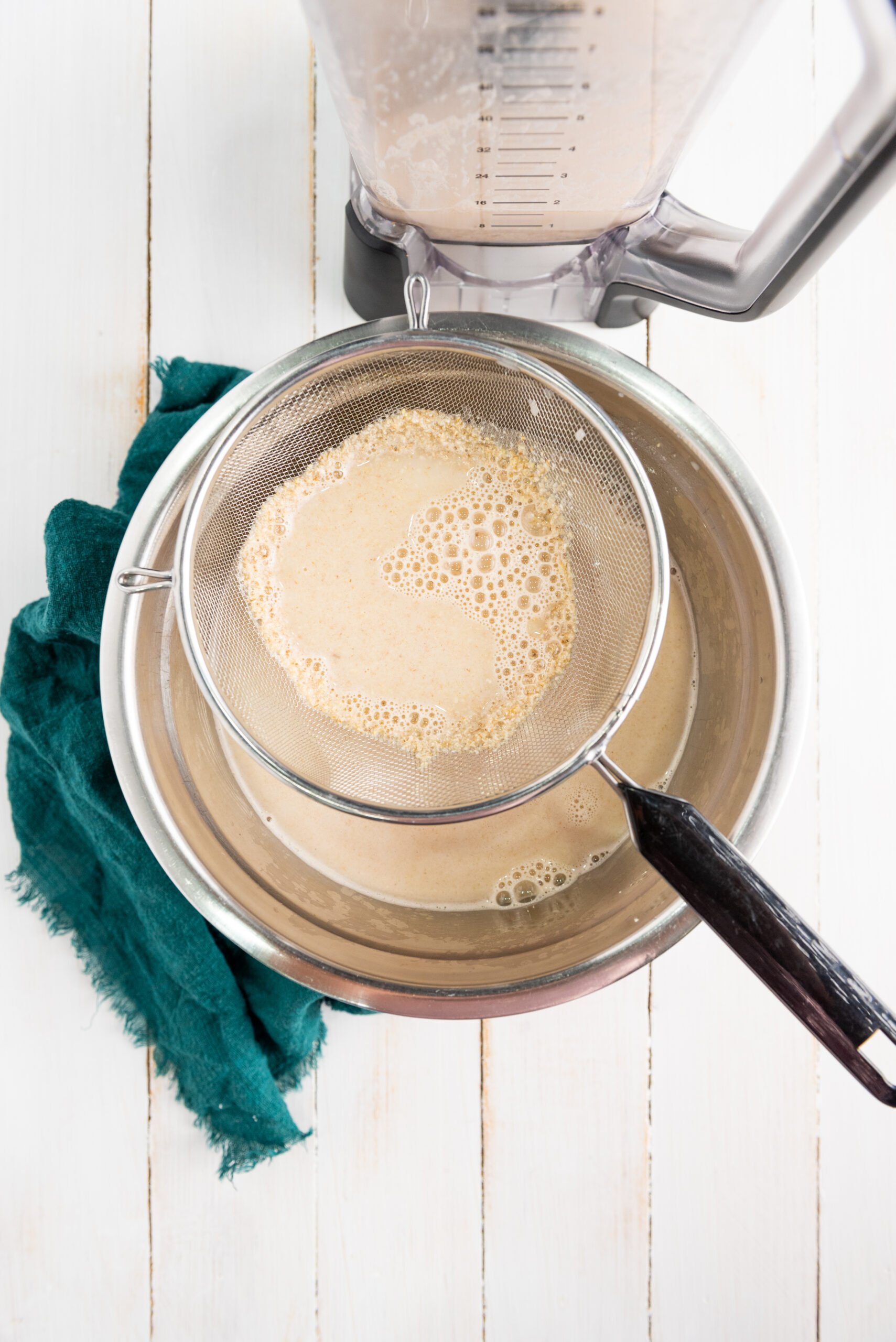 A strainer sits on top of a metal bowl. It is straining gluten-free oat milk.