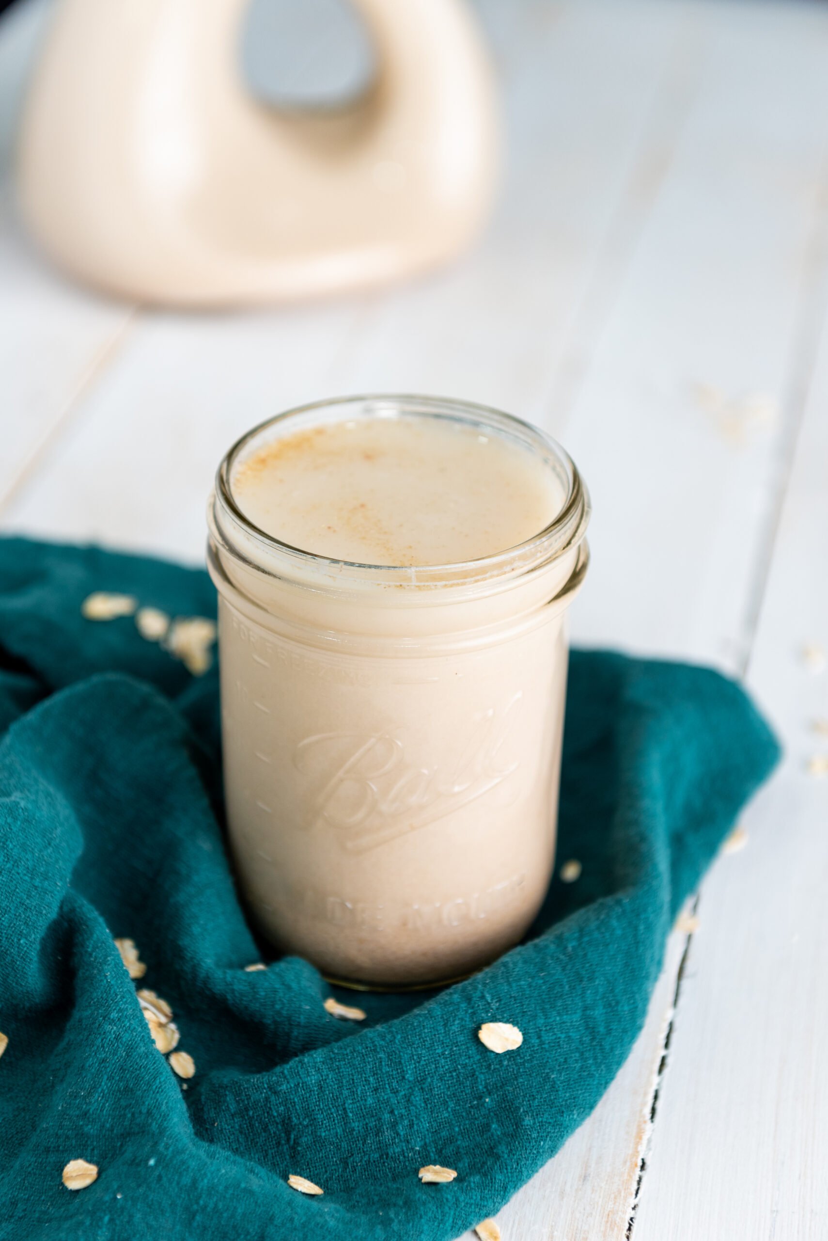 Homemade gluten-free oat milk is in a small jar with a decanter blurred in the background.