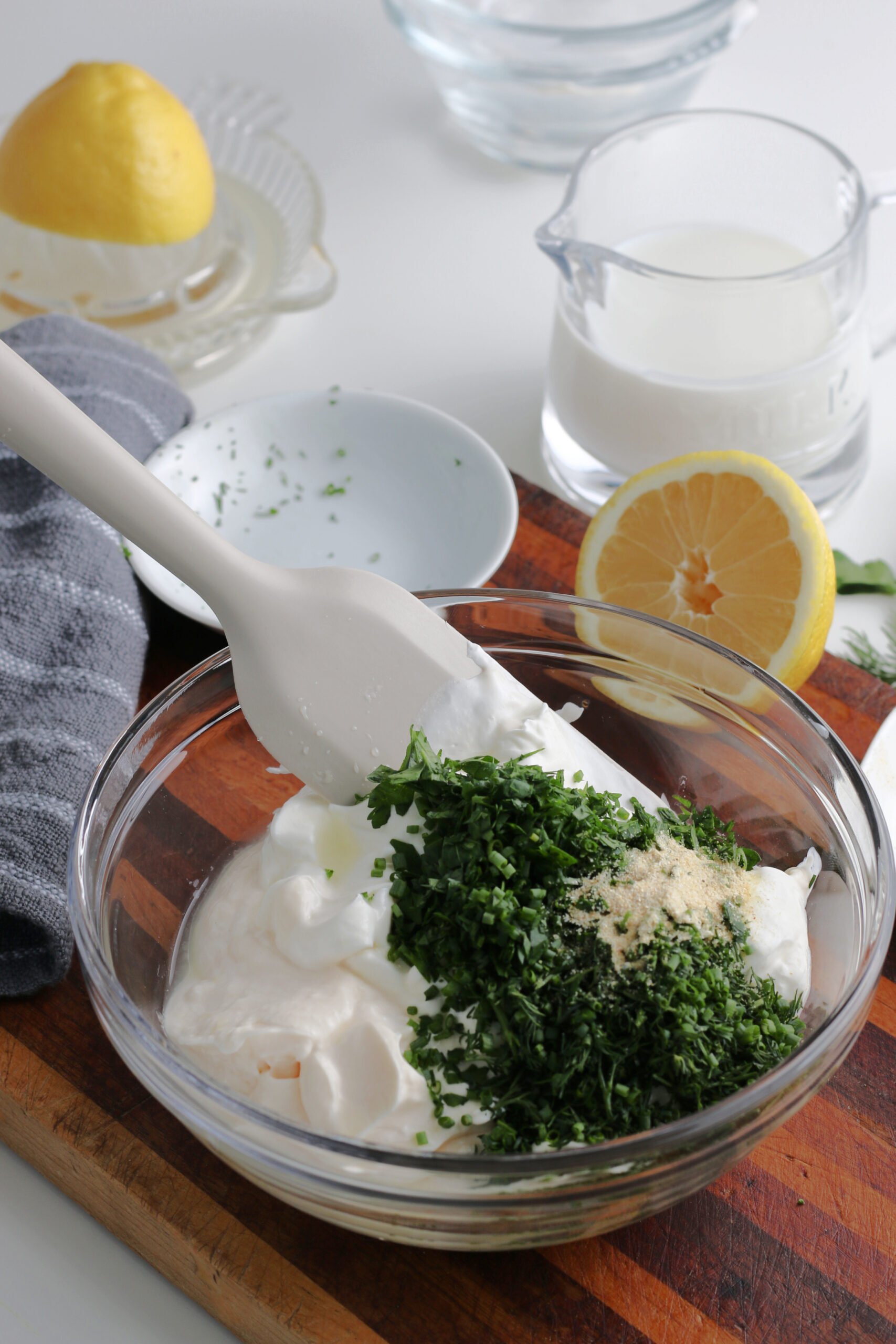 The chopped herbs have been added to the glass bowl of mayonnaise and sour cream.