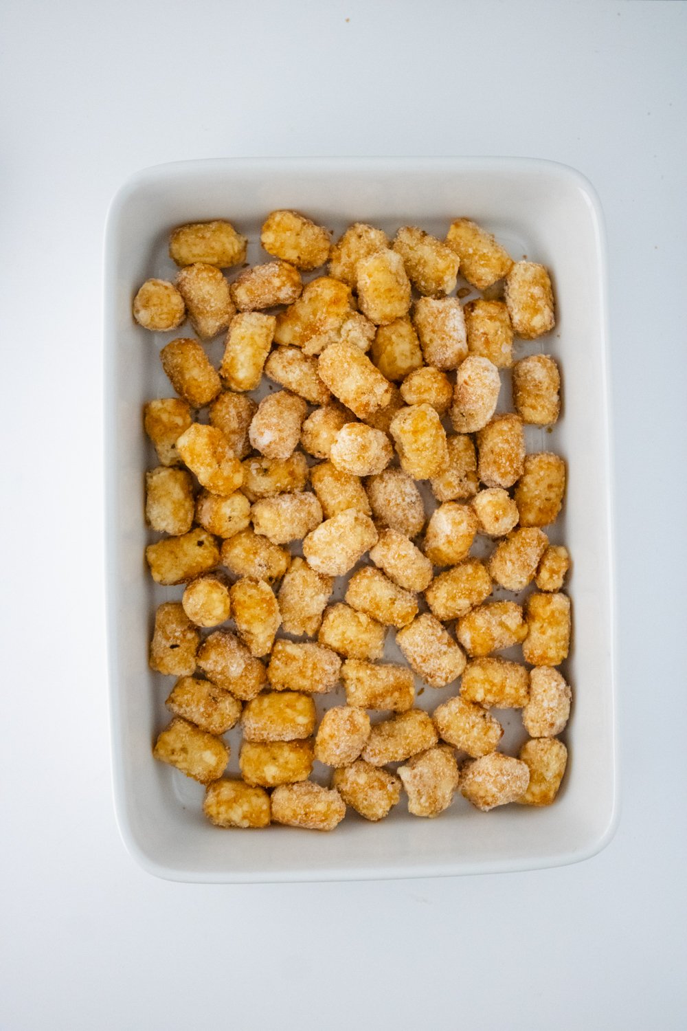 A white casserole dish is covered with a single layer of frozen tater tots.