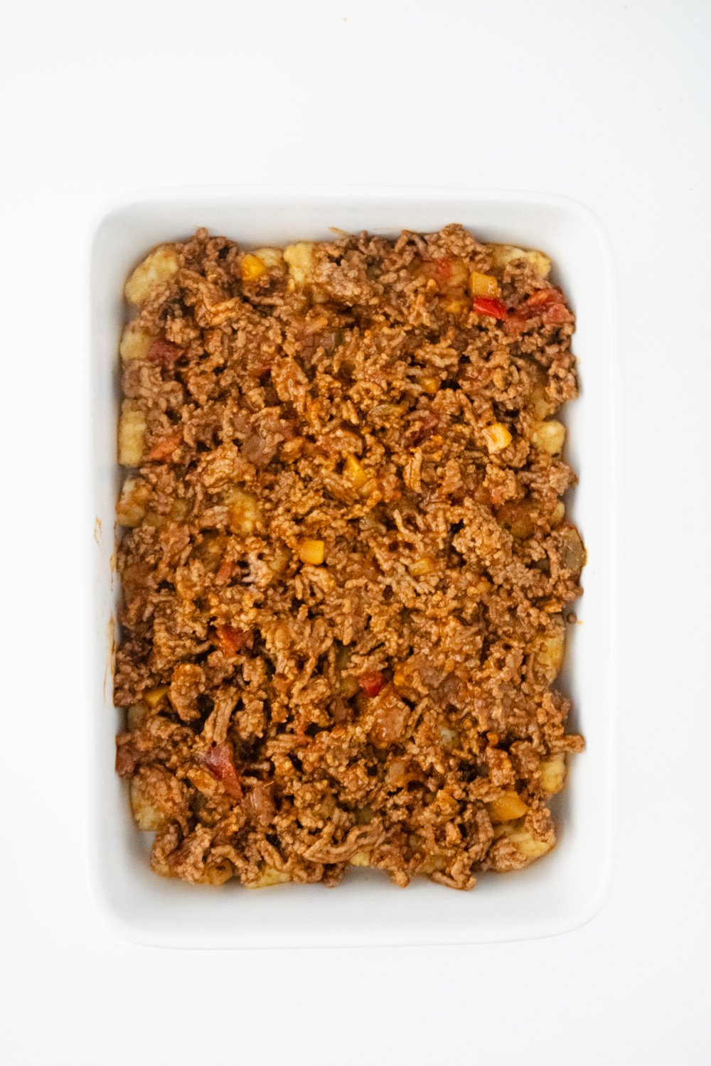 A casserole dish with a layer of tater tots on the bottom is topped with cooked ground beef mixed with salsa.