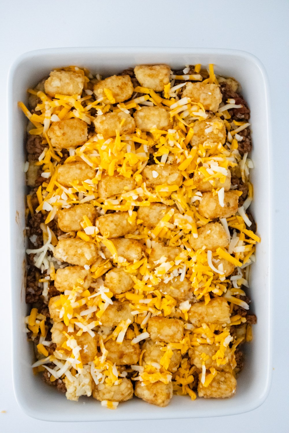 A casserole dish is layered with tater tots, seasoned ground beef, and topped with grated cheese.